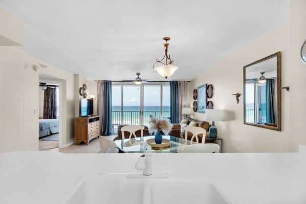 A spacious living area with a large window overlooking the sea, a dining table, and a modern kitchen area.