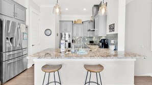 A modern kitchen with stainless steel appliances, a large island with stools, and pendant lighting.