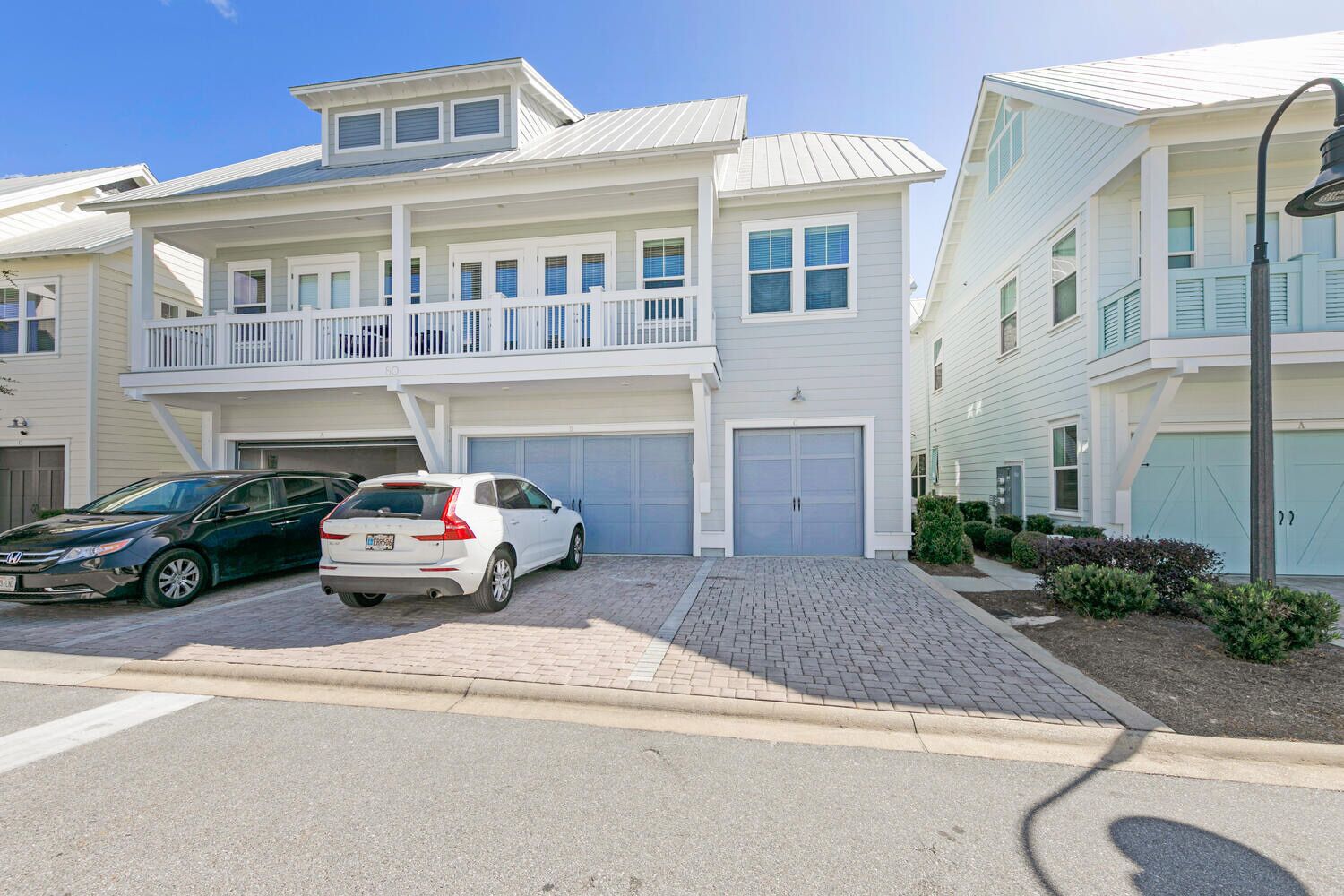 A two-story residential building with a covered garage, a balcony, and a driveway with two cars parked.