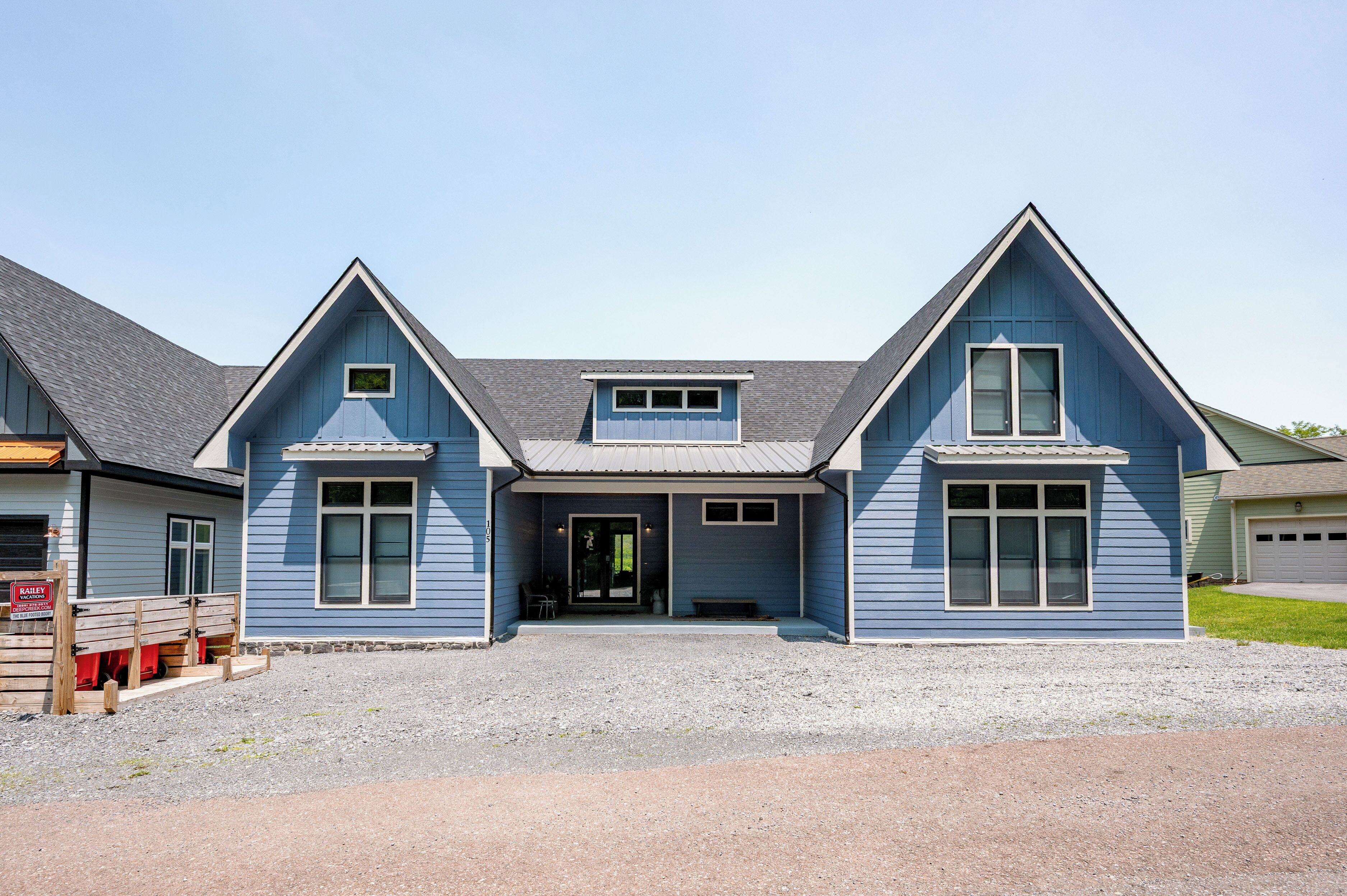 Une maison bleue à deux étages, dotée d’un porche à l’avant, d’un garage et d’une allée gravillonnée.