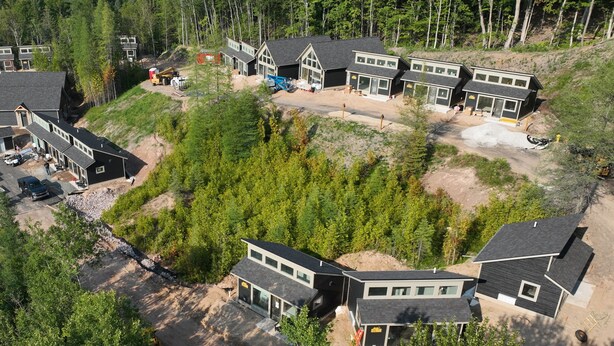 A modern multi-story house with a large driveway, surrounded by dense forest. - EXPLORE Munising Studio Suite 103 (Munising)