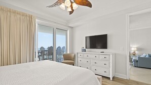 Un dormitorio con una cama grande, ventilador de techo, televisión y vistas al exterior.