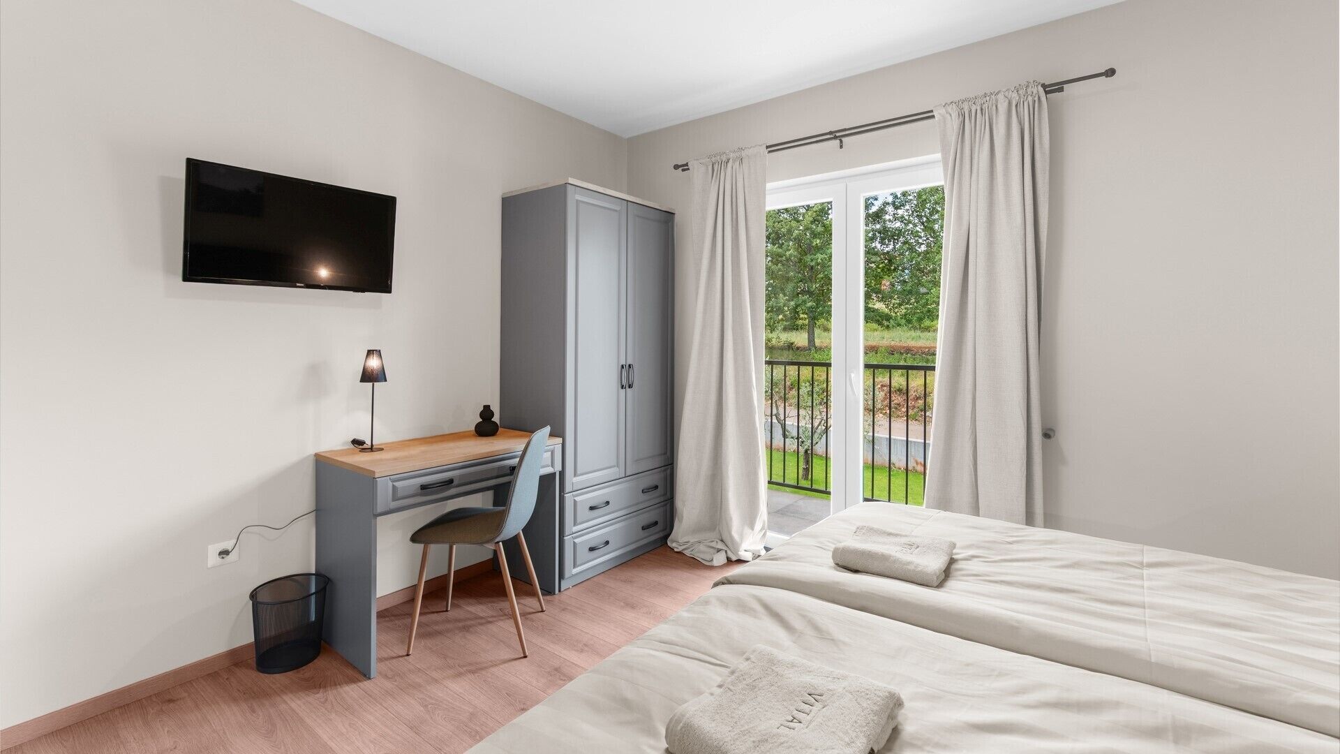 A bedroom with a bed, a desk with a chair, a TV, and a wardrobe.
