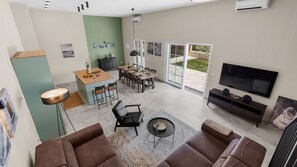 Uma sala de estar moderna com um sofá, uma mesa de centro e uma televisão. Há uma área de jantar com mesa e cadeiras, e uma cozinha com bancada e armários.