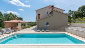 Uma casa de dois andares com piscina, varanda coberta e área de jardim.