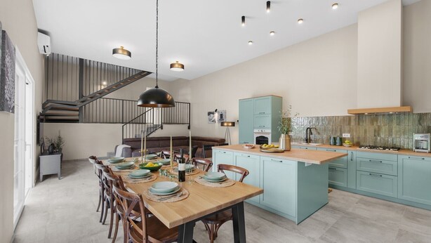 Una cocina moderna con una isla central, armarios azul claro y una escalera que lleva a un nivel superior.