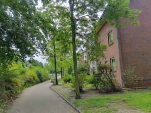 A pathway lined with trees and a brick building with multiple windows. - The most beautiful seagull shore on the North Sea coast, only 3 minutes walk to the beach (Wurster Nordseeküste)