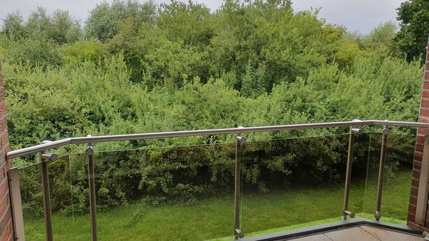Een balkon met een metalen hekwerk, met uitzicht op een gazon en weelderige begroeiing.