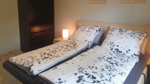 Een slaapkamer met een bed, nachtkastje, lamp en twee kunstwerken aan de muur.