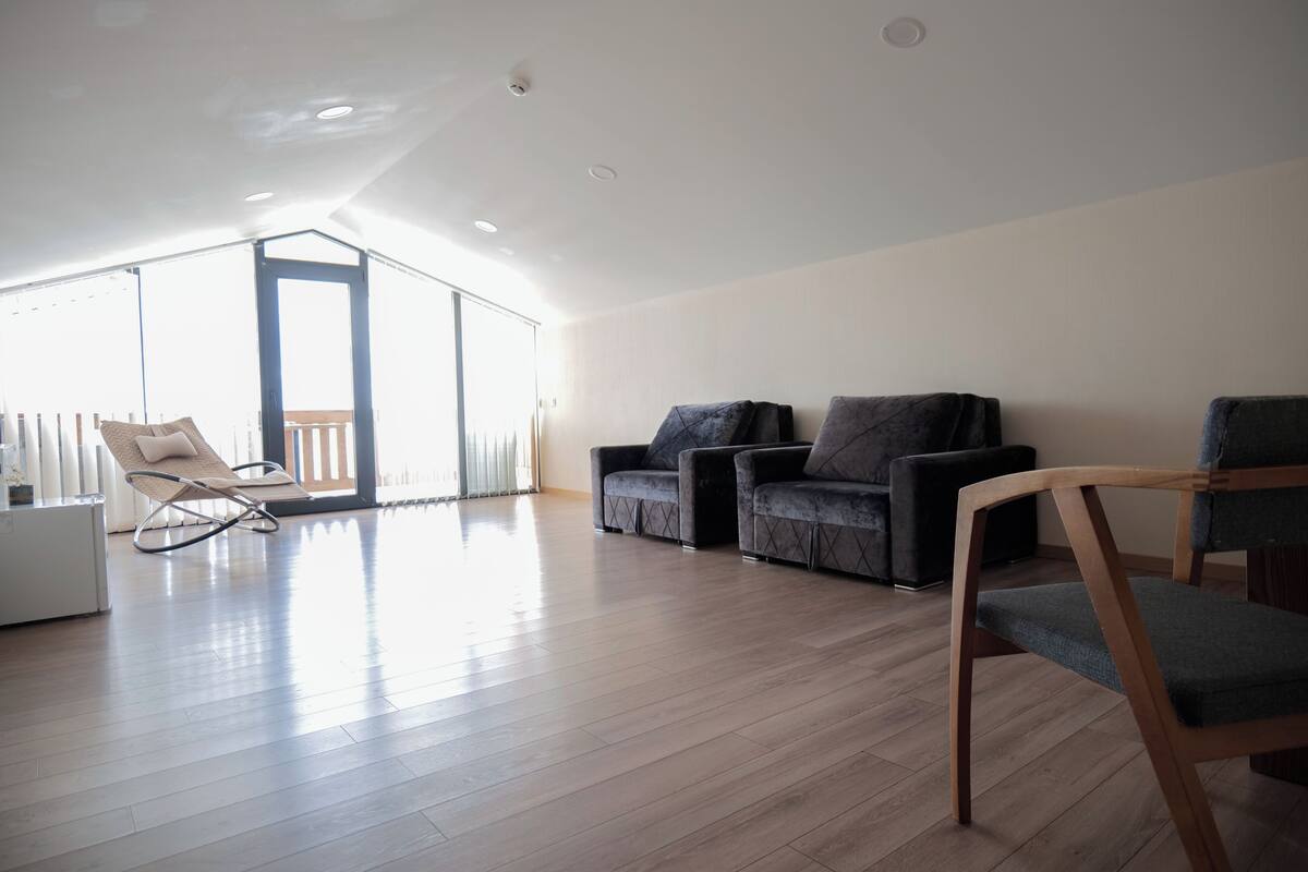 Una habitación amplia con techo alto, un balcón y una zona de estar con sofás y sillones.