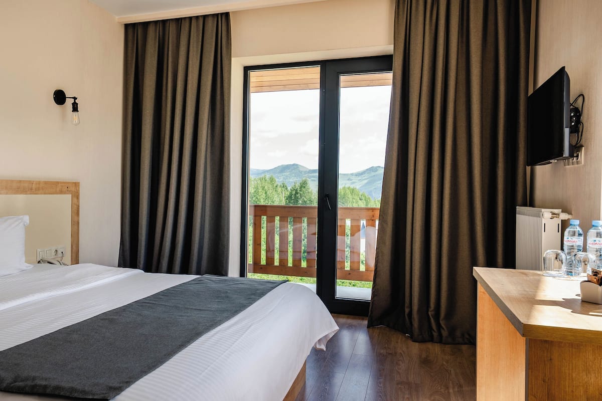 Habitación de hotel con cama, escritorio, televisor y vistas a las montañas desde la ventana.