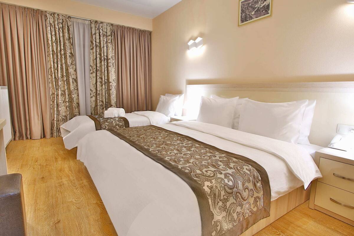 Habitación de hotel con dos camas, una mesita de noche con lámpara, luz de pared e imagen enmarcada.