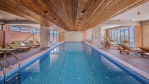 Una piscina interior con vigas de madera en el techo, sillas de descanso y paredes de piedra.