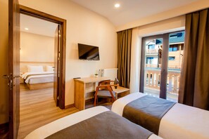 A hotel room with two beds, a desk, a chair, a TV, and a balcony with a view.