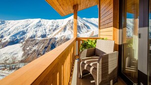 Un balcón con barandilla de madera, muebles de mimbre y vista a montañas nevadas.
