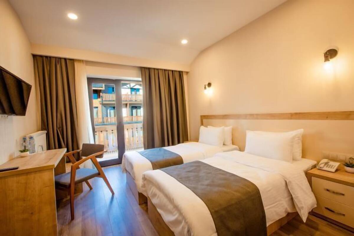 Habitación de hotel con dos camas, un escritorio, una silla, un teléfono y vistas a un balcón.