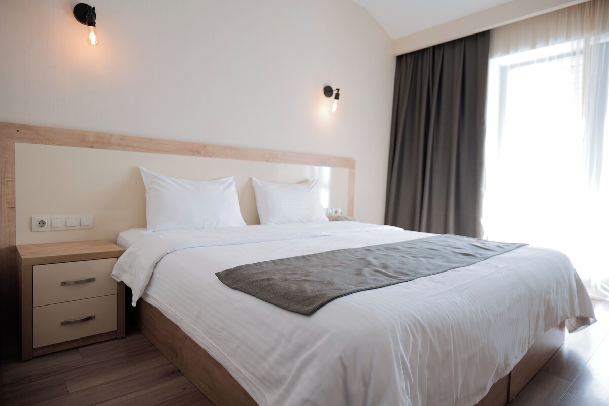 A neatly made bed with a wooden headboard, a bedside table with drawers, and two wall-mounted light fixtures.