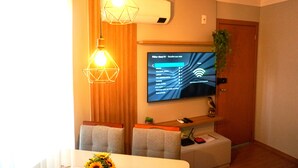 Un salon moderne avec un téléviseur à écran plat fixé au mur, une table à manger avec deux chaises et des luminaires suspendus.