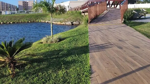 Une promenade en bois menant à un pont qui enjambe une étendue d’eau, avec des bâtiments industriels et un ciel dégagé en arrière-plan.