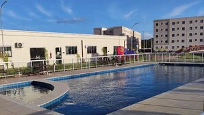 Une piscine sur le toit, avec un ciel bleu dégagé, un bâtiment blanc et une aire de jeux en arrière-plan.
