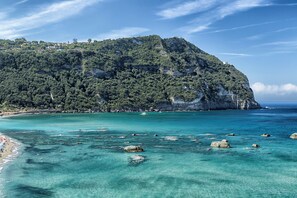 A coastal landscape with a rocky beach, clear turquoise waters, and a forested hill. - Cozy apartment in the heart of Forio d'Ischia equipped with all comforts! (Forio)