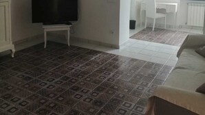 Un salon équipé d’un téléviseur, doté d’un sol carrelé à motifs, comprenant un canapé et une porte en arc donnant sur un coin repas.