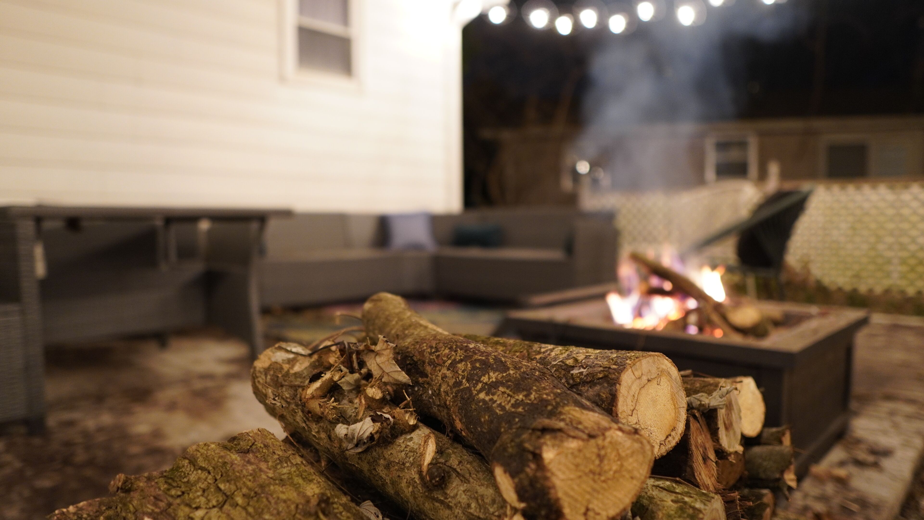 A fire pit with logs and a fire burning, surrounded by a deck area with a sofa and a table.