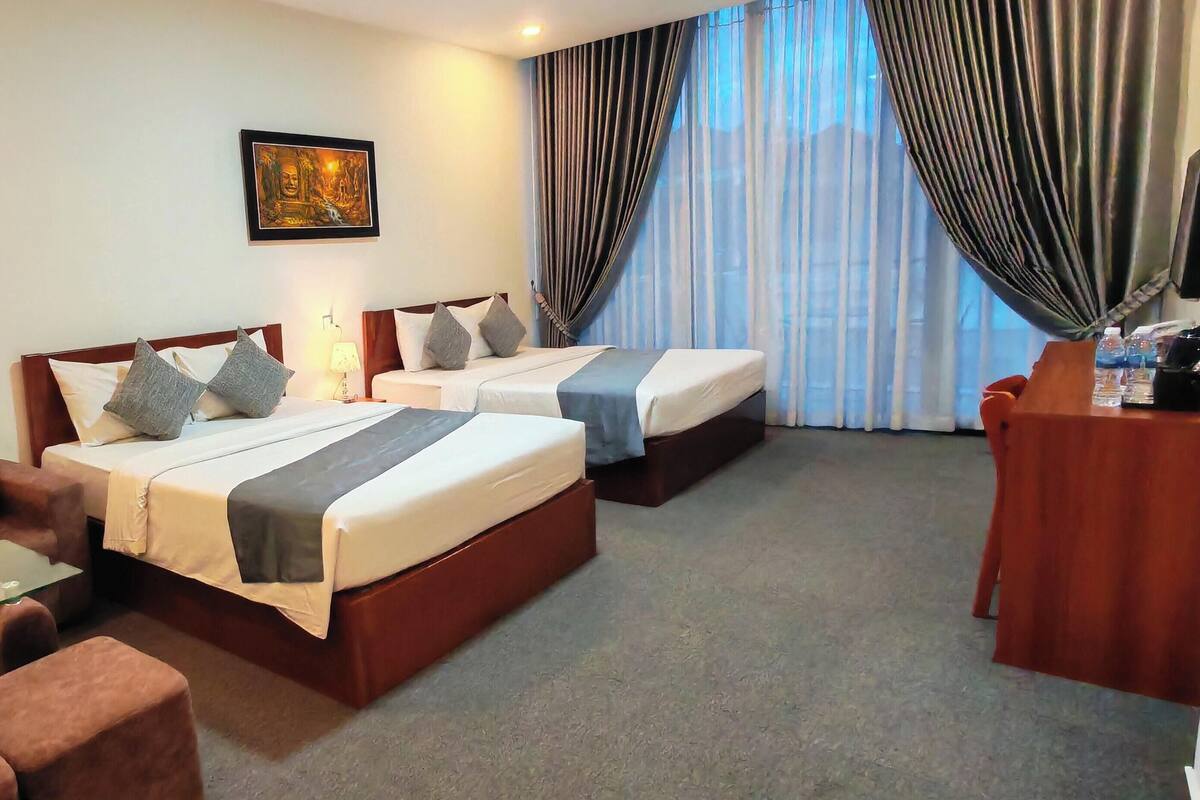 Habitación de hotel con dos camas, un sofá, un escritorio y un ventanal con cortinas.