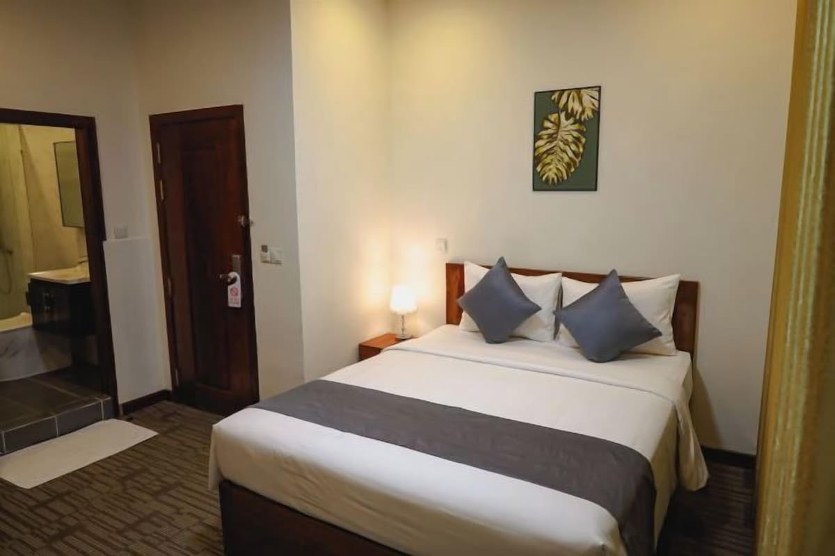 A hotel room with a bed, a nightstand, a wall-mounted artwork, and a door.