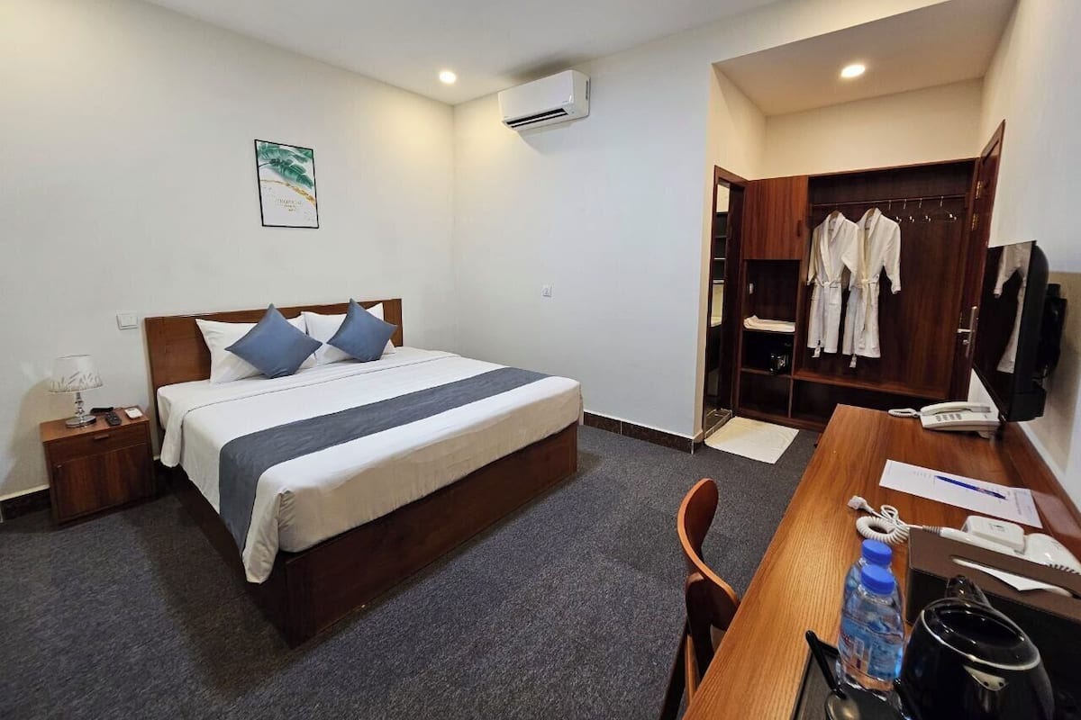 Habitación de hotel con cama, mesita de noche, escritorio, silla, armario y equipo de aire acondicionado.