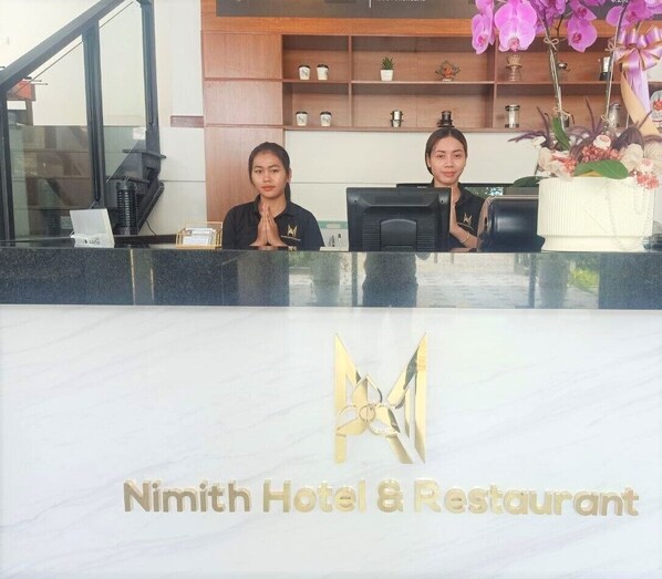 A reception desk at Nimith Hotel & Restaurant with a marble countertop and a logo.