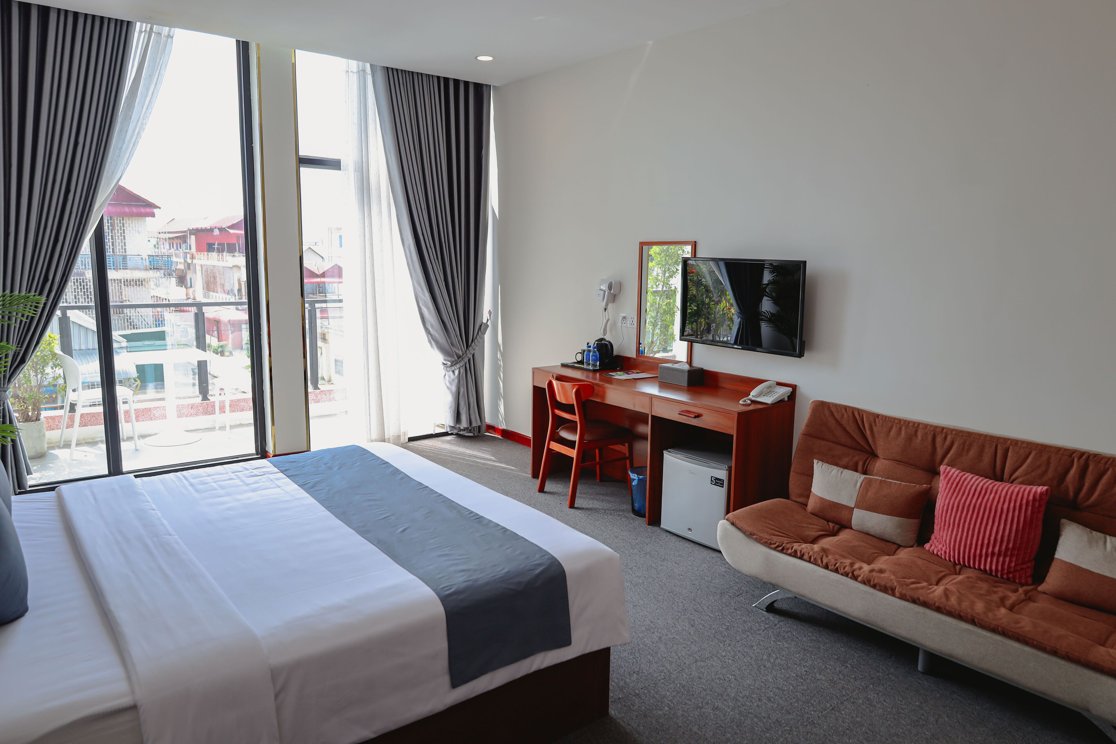 Habitación de hotel con cama, escritorio, sofá, televisión y vistas a edificios.