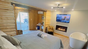 A log cabin-style bedroom with a bed, a chair, a fireplace, and a television. - Auberge du Vieux Moulin (Sainte-Emelie-de-L'Energie)