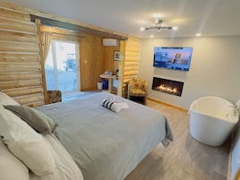 A log cabin-style bedroom with a bed, a chair, a fireplace, and a television.