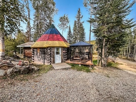 A rustic cabin with a colorful conical roof, surrounded by a forest.