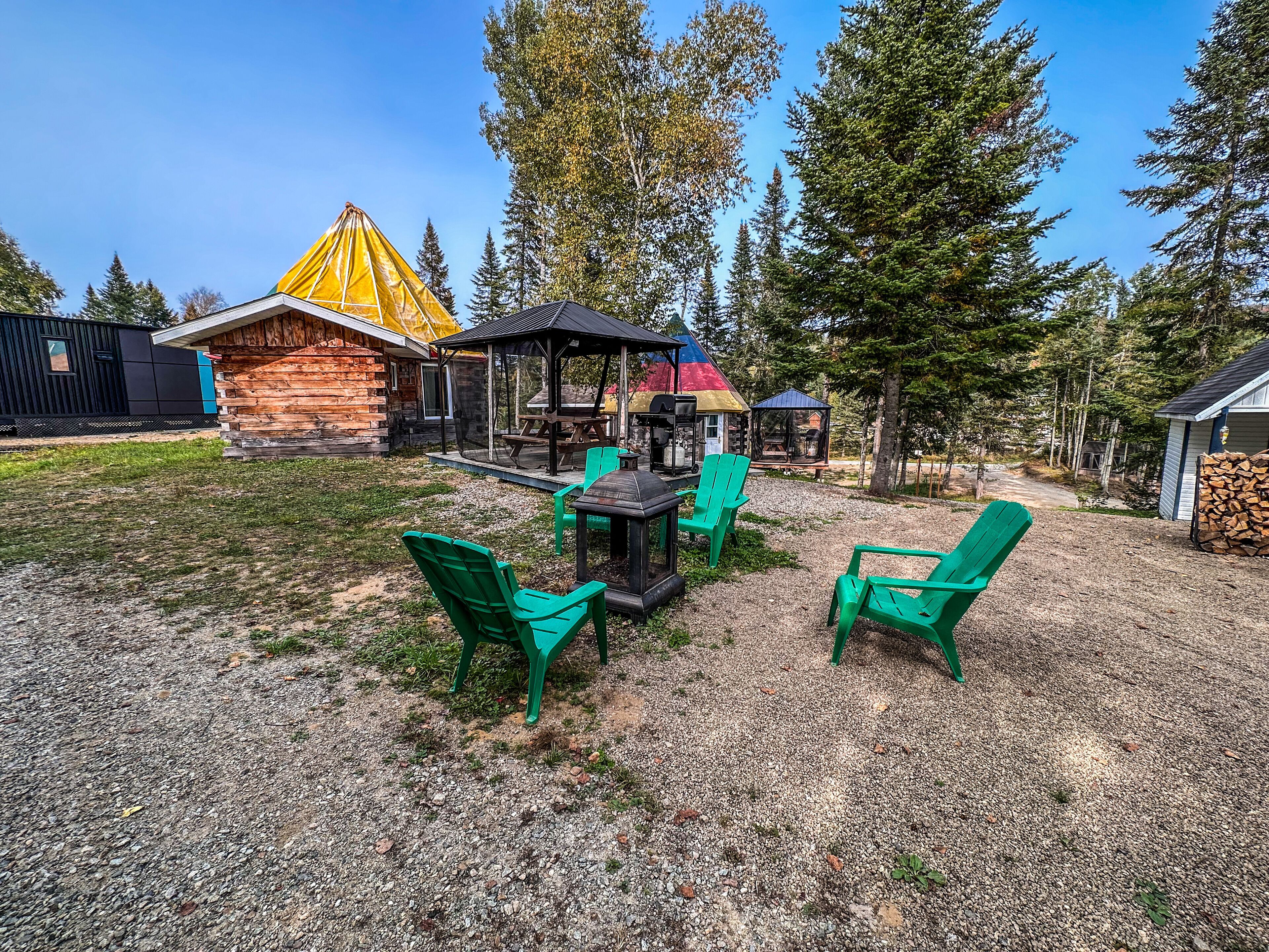 A rustic cabin with a wooden exterior, a covered outdoor seating area with chairs, and a picnic table.