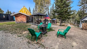 A rustic cabin with a wooden exterior, a covered outdoor seating area with chairs, and a picnic table.