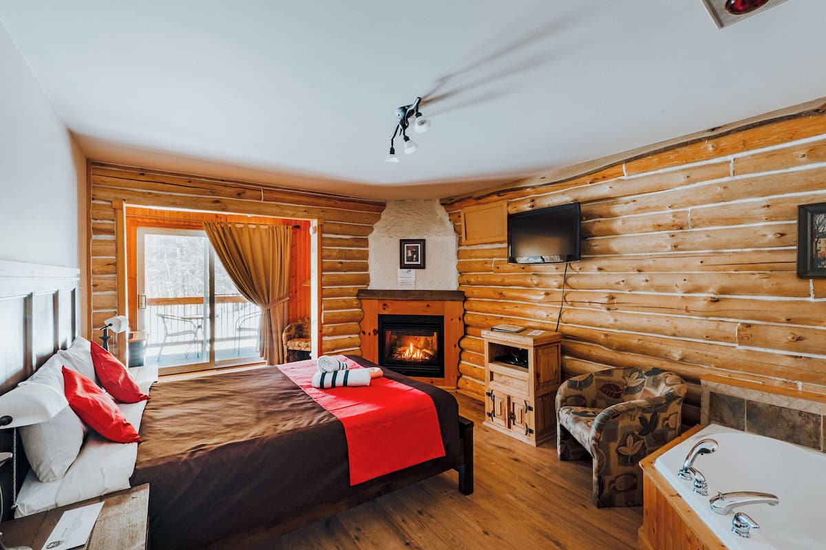 Um quarto em estilo cabana de tronco com uma cama, lareira, televisão e uma pequena mesa com uma cadeira.