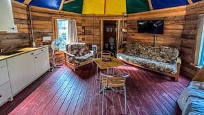 A cozy interior of a wooden cabin with a dining area, sofa, and kitchenette. - Auberge du Vieux Moulin (Sainte-Emelie-de-L'Energie)