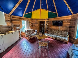 A cozy interior of a wooden cabin with a dining area, sofa, and kitchenette.