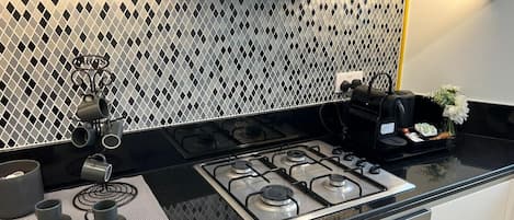 Una cocina con estufa a gas, cafetera y juego de té sobre la encimera.