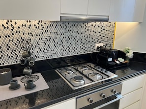A kitchen with a gas stove, a coffee maker, and a tea set on the counter.