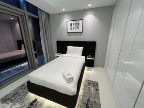 Quarto de hotel moderno com uma cama grande, uma mesa de cabeceira, uma TV fixada na parede e uma janela com vista para o exterior.