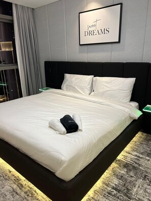 A neatly made bed with white linens and a rolled towel, a framed sign above stating 'sweet DREAMS', and a dark headboard.
