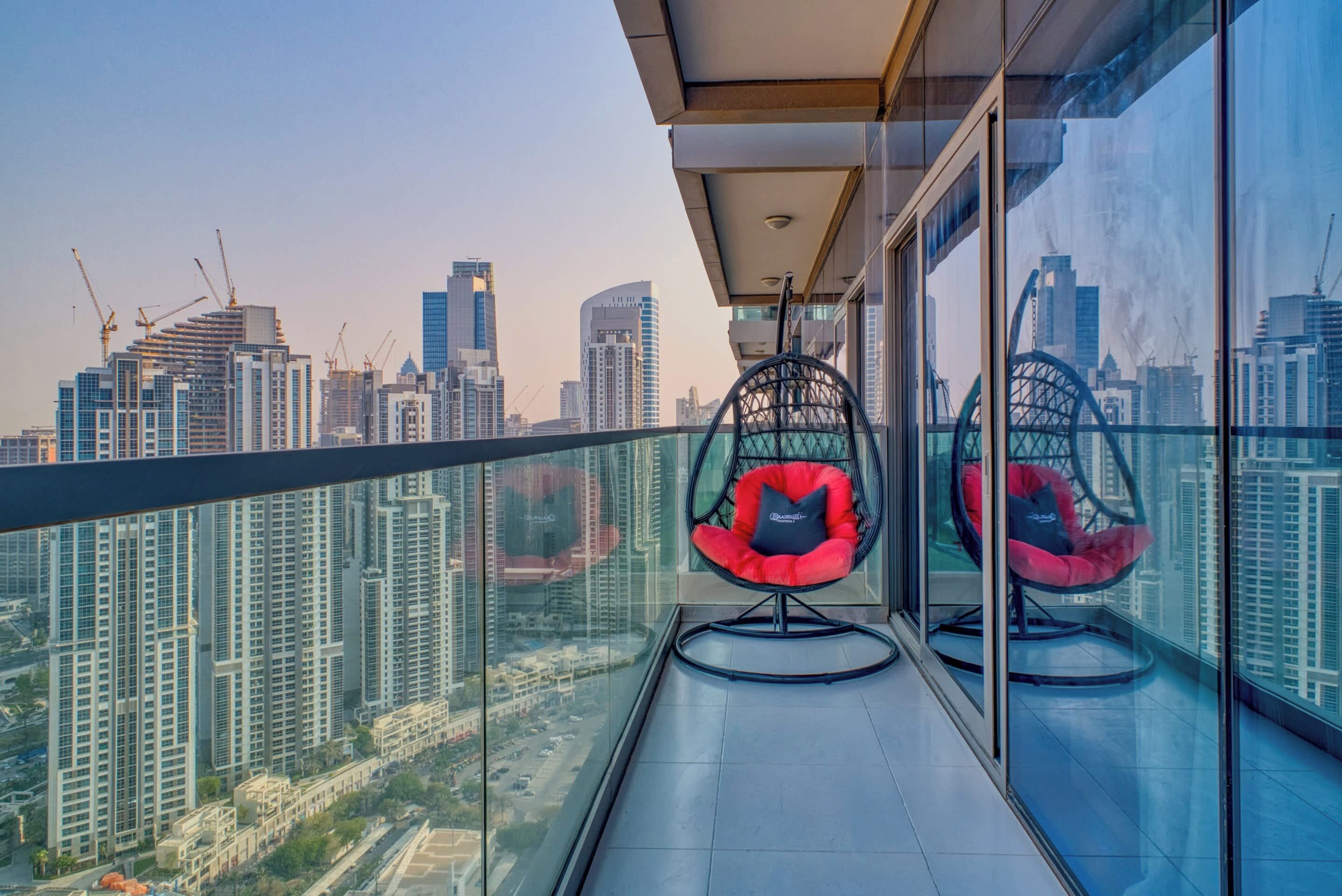 Un balcon avec vue sur la ville, deux chaises rouges et une rambarde en verre.