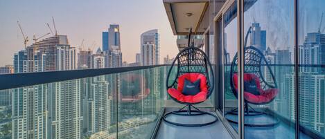 Un balcon avec vue sur la ville, deux chaises rouges et une rambarde en verre.