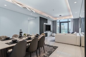 A modern dining area with a long table, chairs, and a TV mounted on the wall. - Quasi-Homes | Paramount Midtown 3BR, Pool & Gym (Dubai)