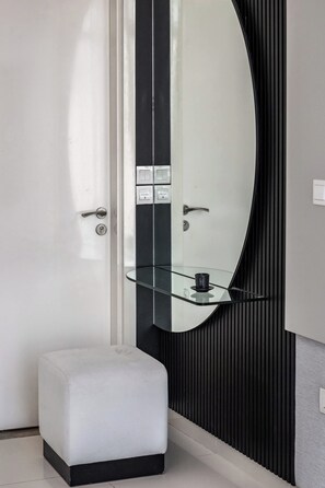 A modern bathroom with a glass shelf, a white bench, and a large mirror.
