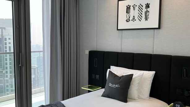 Moderni hotellihuone, jossa on suuri sänky, näköala kaupunkiin ja seinällä oleva taulu.