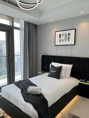 A modern hotel room with a large bed, a city view, and a framed picture on the wall.